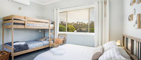 Un dormitorio con una litera, una cama individual, una ventana con persianas y vistas al exterior.
