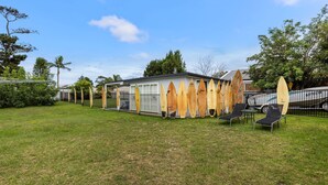 Ein Haus mit überdachter Terrasse, einem Rasen und mehreren Surfbrettern, die an einem Zaun angelehnt sind.