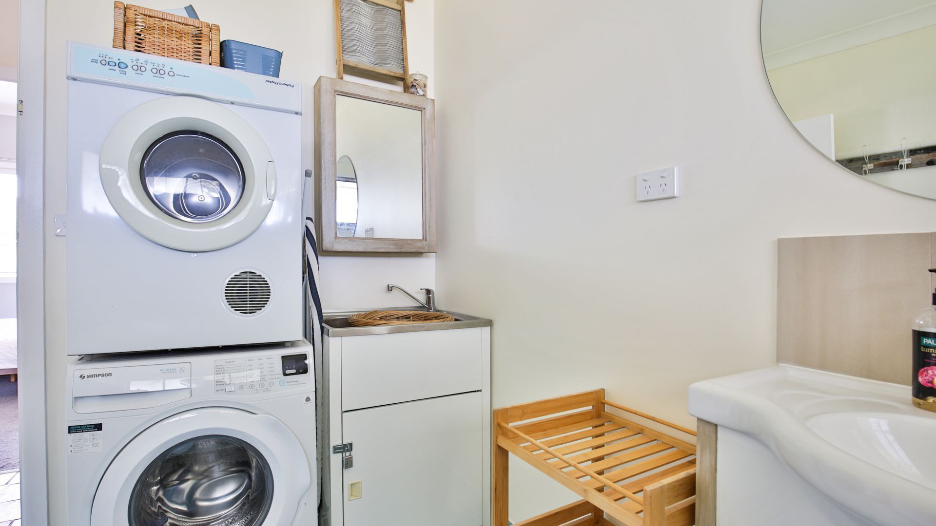 Een wasserette met gestapelde wasmachines, een wasbak en een houten droogrek.