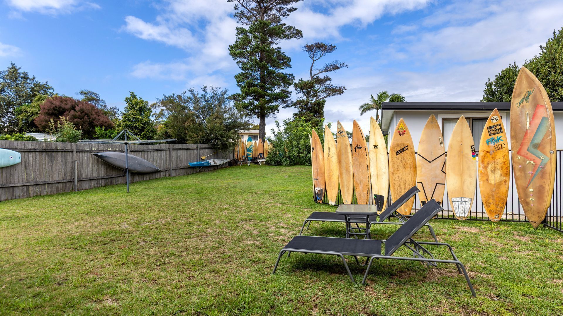 A backyard with a wooden fence, a small shed, and several surfboards leaning against it.