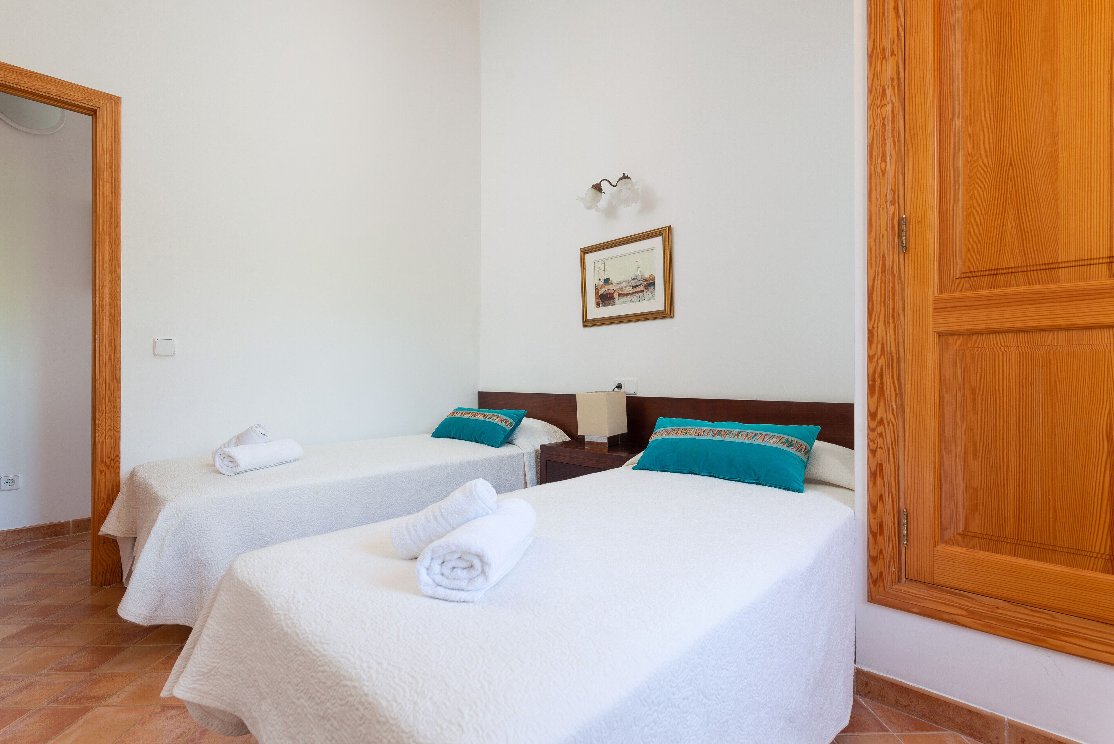 Habitación de hotel con dos camas, ropa de cama blanca, almohadas color turquesa, un cuadro en la pared y un armario de madera.