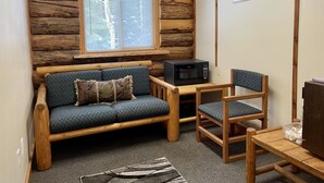 A cozy cabin-style room with a wooden log wall, a sofa with patterned cushions, a small table with a microwave, a chair, and a rug. - Rustic log cabin (Naples)