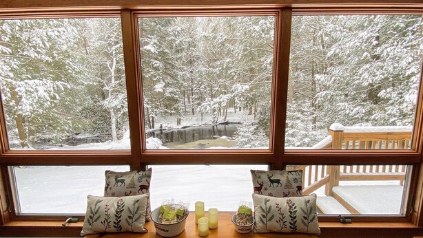 Una ventana con vista a un bosque nevado y una terraza de madera.