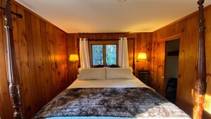Un dormitorio con paneles de madera, una cama con dosel, dos lámparas de noche y un ventanal con cortinas.