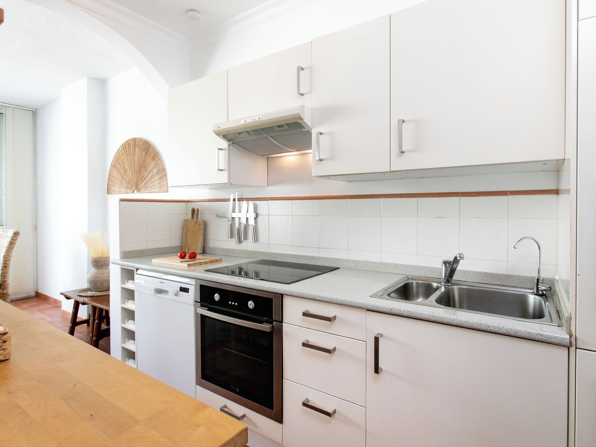A modern kitchen with white cabinetry, a stainless steel sink, and a built-in oven.