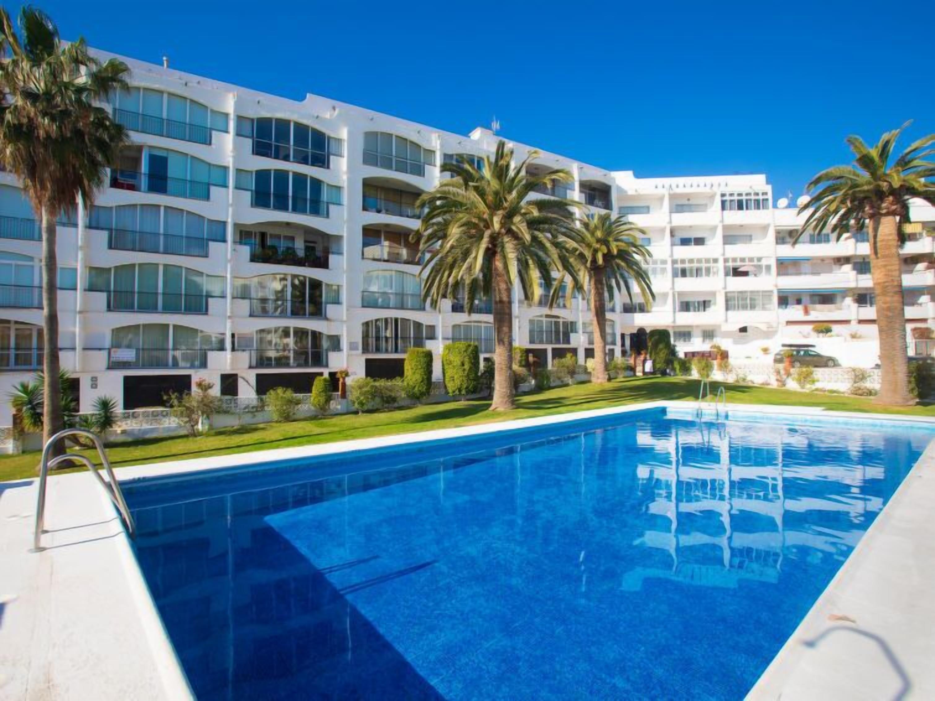 Un hôtel moderne doté d’une piscine, de palmiers et surplombant un ciel d’un bleu limpide.