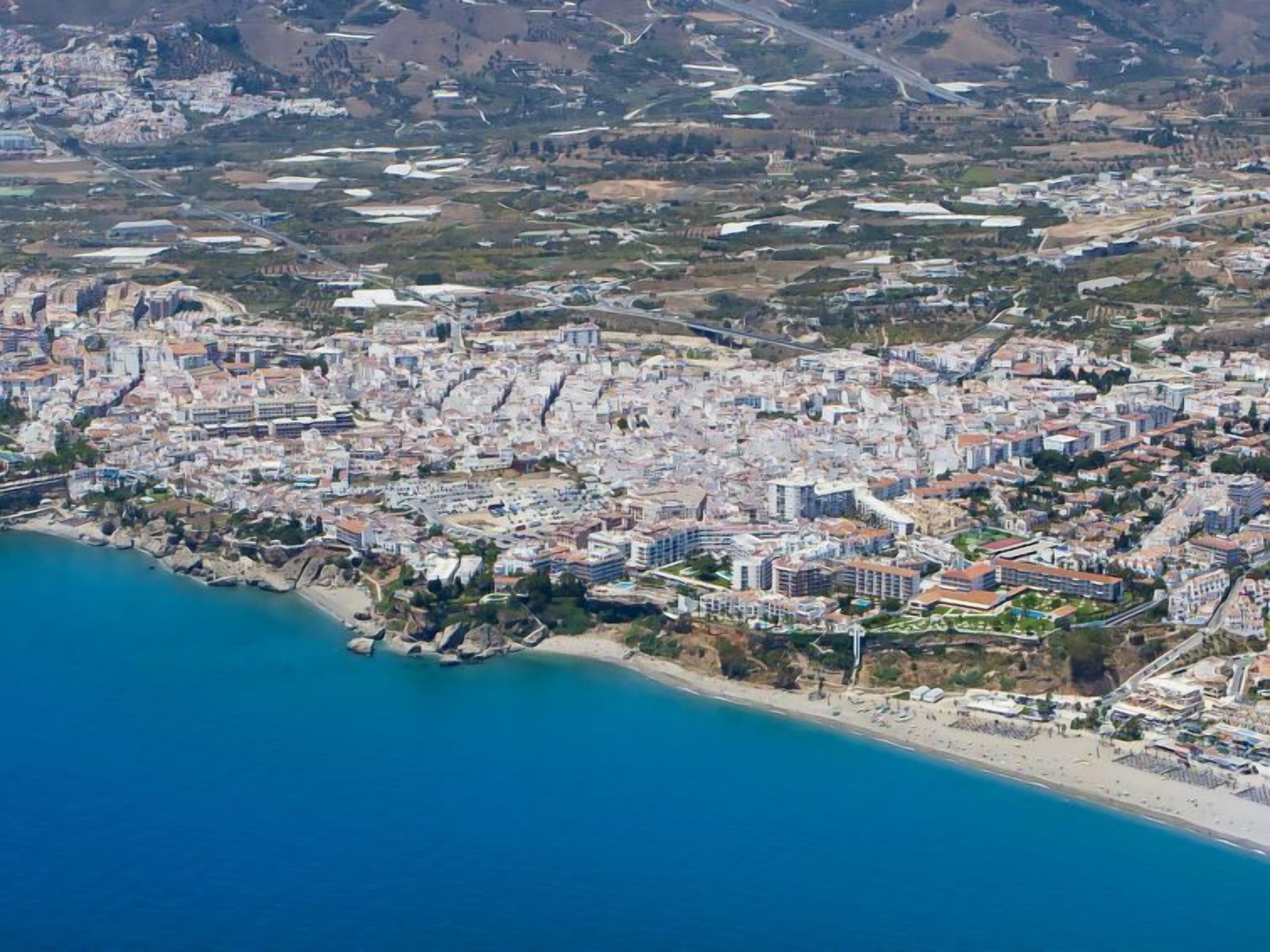 An aerial view of a coastal city with dense urban development, a beach, and a mix of residential and commercial buildings.