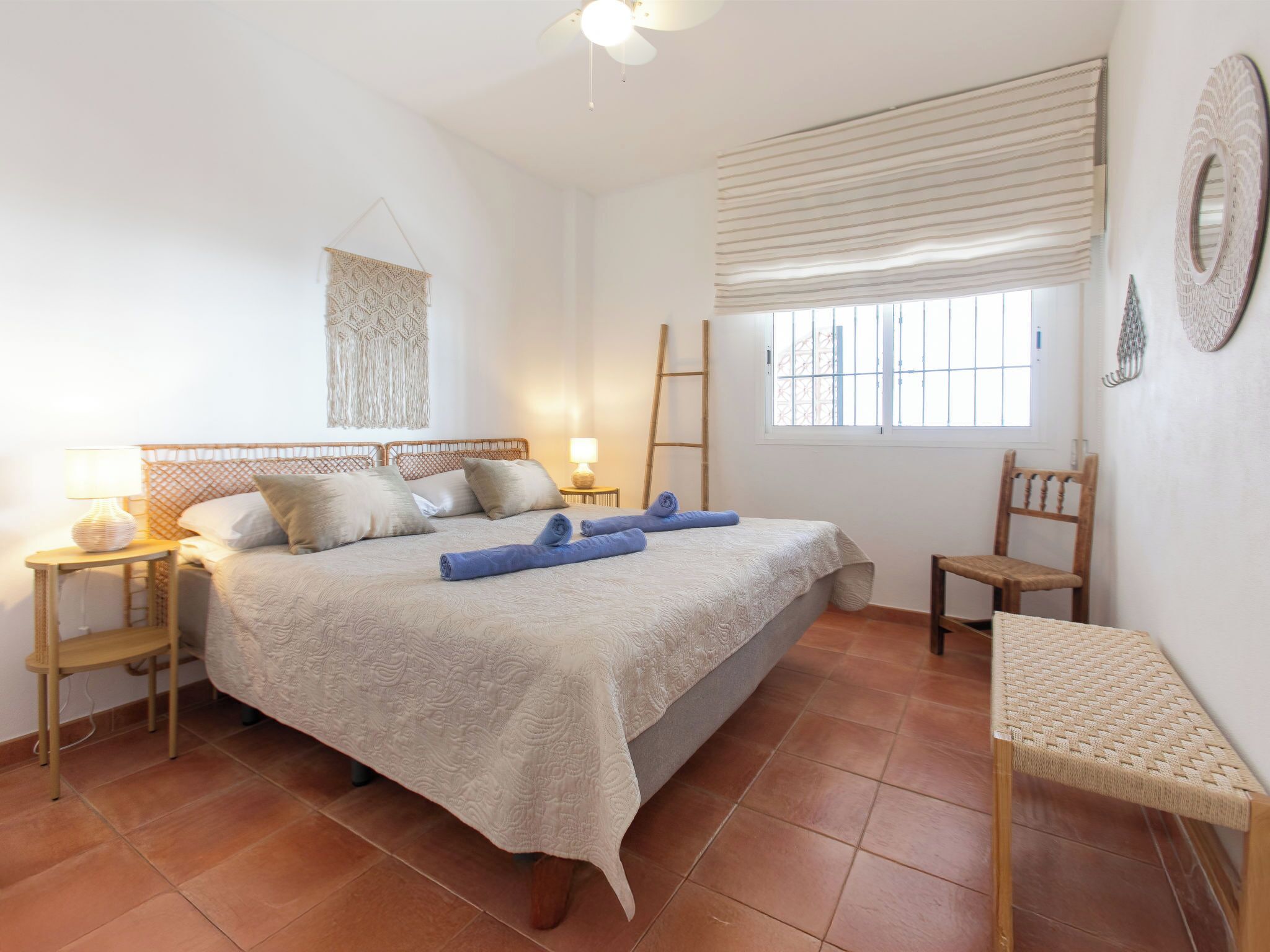 Un dormitorio con cama, mesita de noche, silla, ventana con persianas y un adorno en la pared.