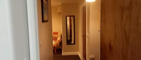 Un pasillo con piso alfombrado, una puerta de madera y una lámpara.
