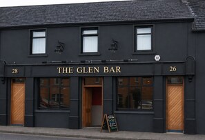 A black building with 'THE GLEN BAR' sign, two windows, and a wooden door.