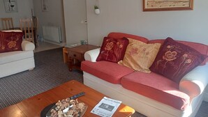 Ett vardagsrum med en röd soffa, ett träbord och en tavla som föreställer en strandvy.