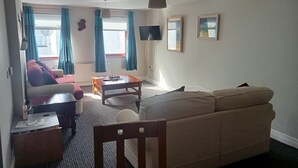 Ett vardagsrum med en soffa, ett soffbord, en tv och ett fönster med gardiner.