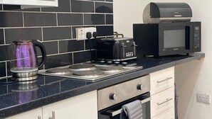 A modern kitchen with a gas stove, a kettle, a coffee maker, and a microwave. - 2 Bed Flat - Sleeps 6 - Parking - Wifi (Bridgend)