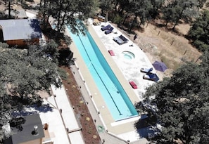 Vue aérienne d’une piscine entourée d’arbres, avec des chaises longues et un jacuzzi.