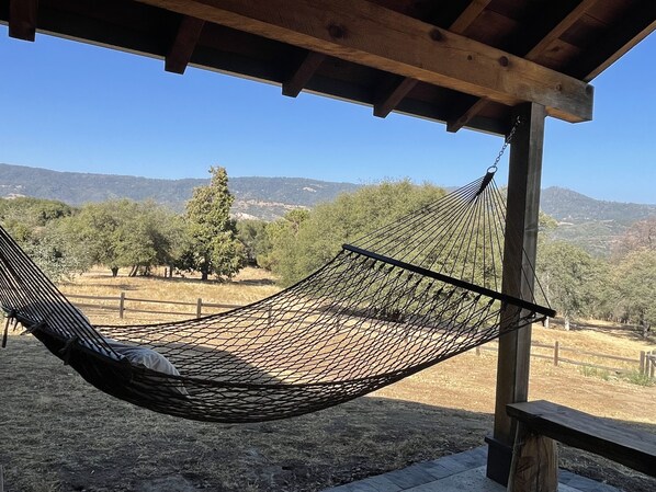Un hamac sous une pergola en bois, avec vue sur les arbres et les montagnes.