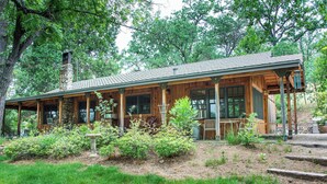 A wooden cabin with a porch, surrounded by greenery and trees. - Starview Ranch: 3 homes w/ 7 bdrms, pool, sauna, spa & gym on 50 beautiful acres (Miramonte)