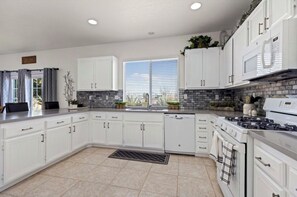 Uma cozinha moderna com armários brancos, fogão embutido e uma janela grande que proporciona iluminação natural.