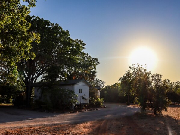 A white house with a dirt driveway, surrounded by trees and a clear sky.