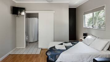 A modern hotel room with a bed, a TV mounted on the wall, a window with a view of trees, and a door leading to a bathroom.