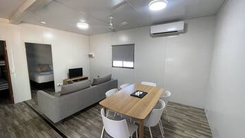 A compact living space with a sofa, a TV, a dining table with chairs, and an air conditioning unit.