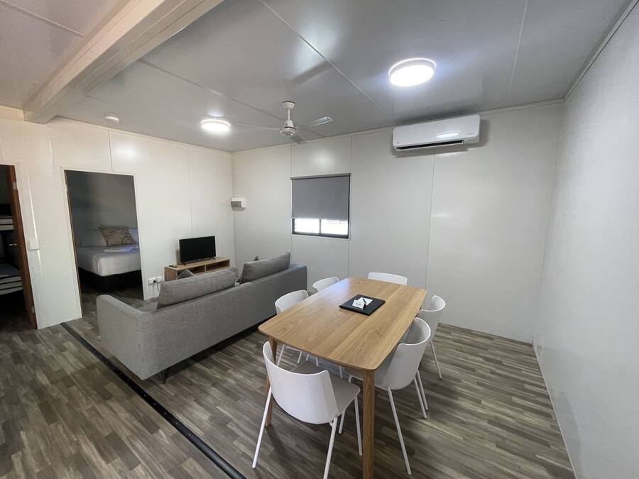 A compact living space with a sofa, a TV, a dining table with chairs, and an air conditioning unit.