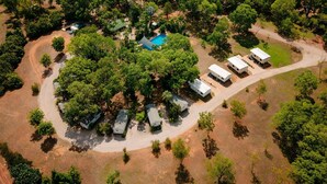 An aerial view of a campground with several RVs, a swimming pool, and dense surrounding trees.
