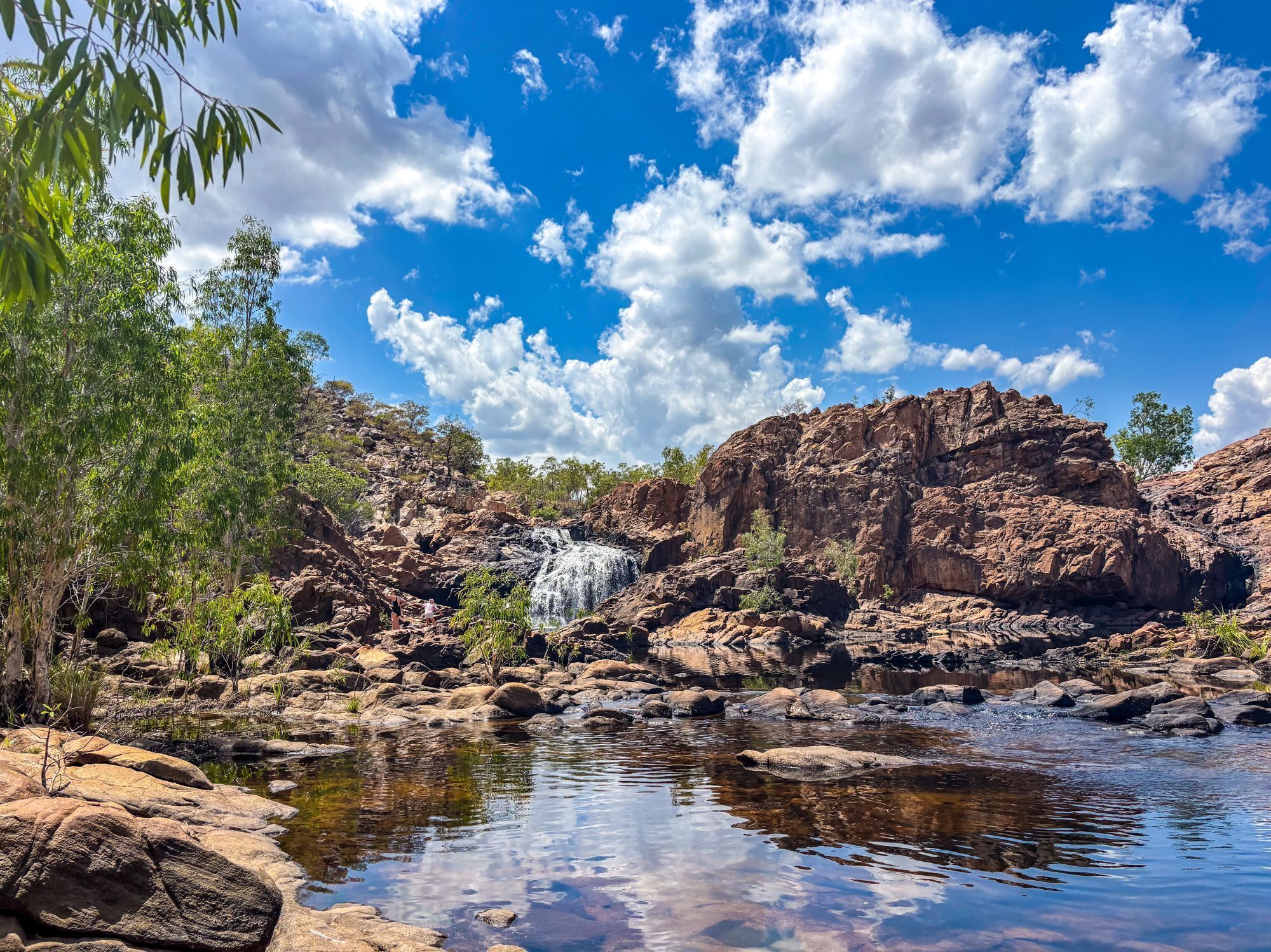 Eine natürliche Landschaft mit einem Wasserfall, felsigem Gelände und blauem Himmel.