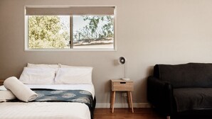 A bedroom with a bed, bedside table, lamp, and a black sofa.