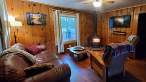 A cozy cabin interior with a wooden interior, a fireplace, a sofa, a chair, and a television. - Cottage #2 with a Lake and Creek, 15 mi to Lassen NP (Shingletown)