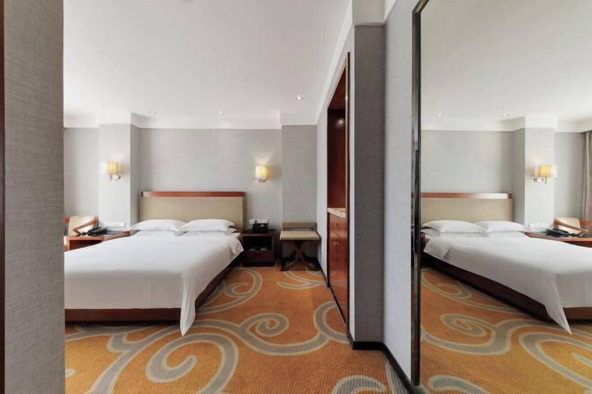 A hotel room with two beds, a carpeted floor, and a mirror reflecting the room.