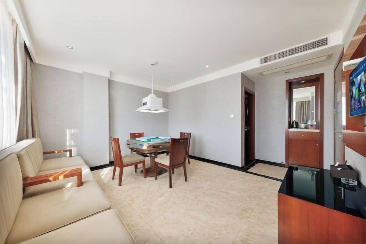 A modern hotel room with a sofa, dining table, and chairs. There is a TV on the right side.