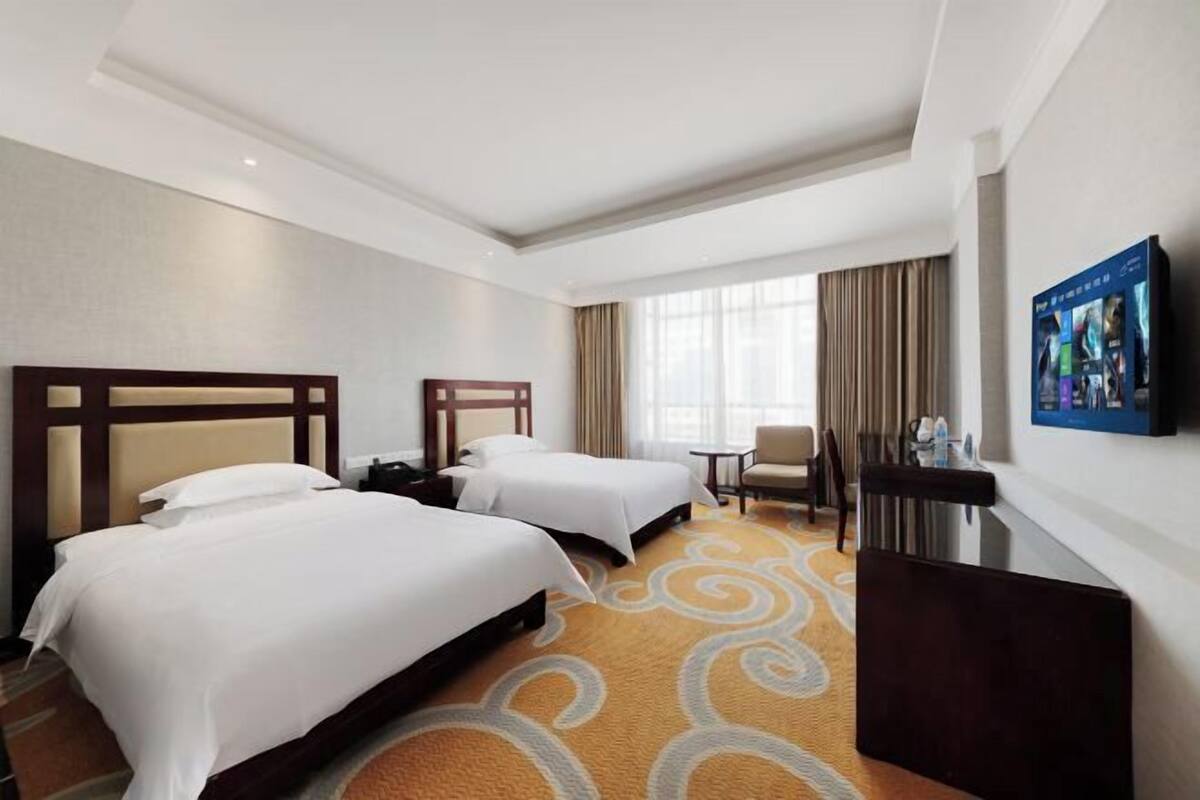 A hotel room with two beds, a desk, a chair, and a television on the wall.
