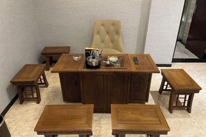 A wooden dining set with a central table and four matching stools, a beige upholstered chair, and a small side table with a teapot and cup.