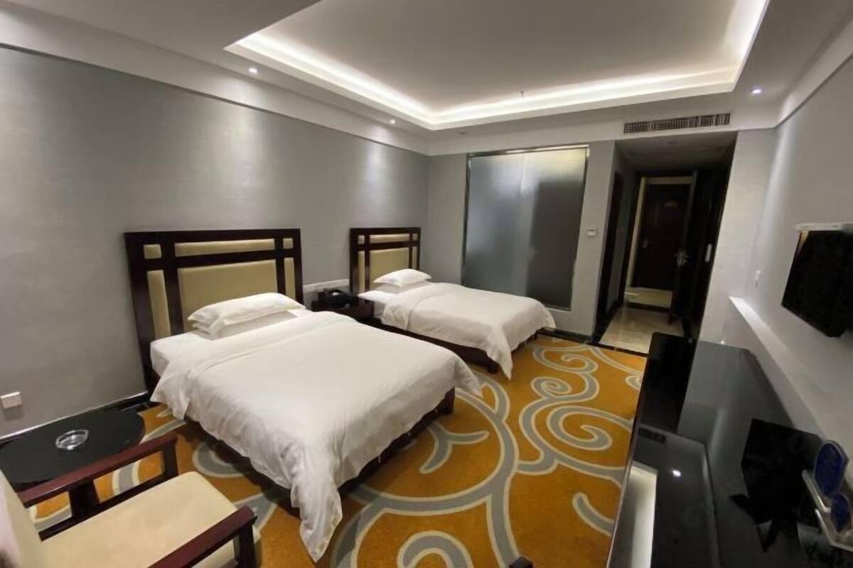 A hotel room with two beds, a desk, a chair, and a TV.
