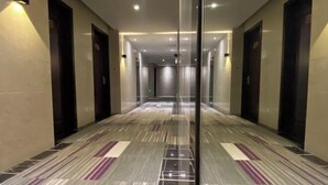 A long, narrow hallway with a patterned carpet, doors on both sides, and recessed lighting.