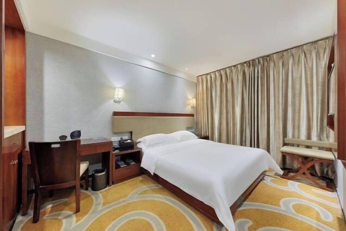A hotel room with a bed, desk, chair, and a curtain.