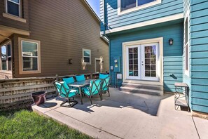 Eine Terrasse mit Tisch und Stühlen, eine kleine Sitzgelegenheit im Freien, und ein Haus mit blauer Fassade und braunen Verkleidungen.