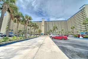 A large hotel with multiple floors, a parking lot with several cars, and palm trees lining the street.