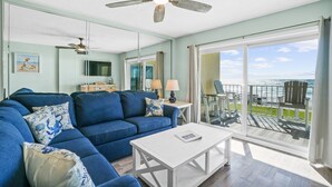 A living room with a blue sofa, white coffee table, and a view of the ocean through large glass doors. - 2nd Floor Beachfront Getaway | Regency Towers, Pools, Tiki Bar & Gulf Views (Panama City)