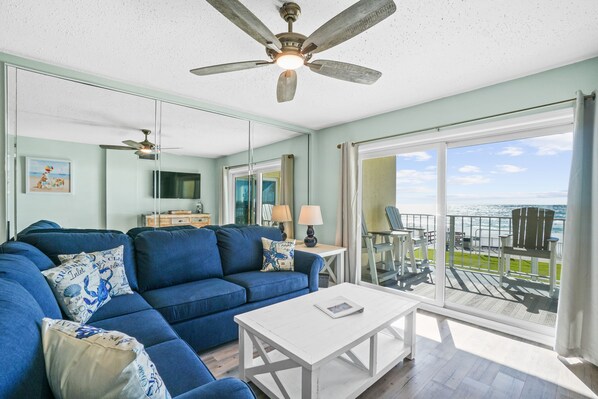 A living room with a blue sofa, white coffee table, and a view of the ocean through large glass doors.