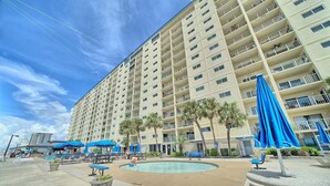 A multi-story hotel with a pool area, outdoor seating, and palm trees. - 2nd Floor Beachfront Getaway | Regency Towers, Pools, Tiki Bar & Gulf Views (Panama City)