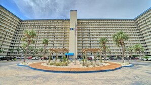 A large, multi-story hotel with a central courtyard featuring palm trees and a pergola. - 2nd Floor Beachfront Getaway | Regency Towers, Pools, Tiki Bar & Gulf Views (Panama City)