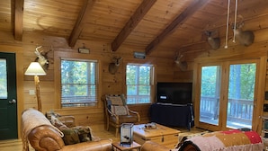 Interior de una cabaña con paredes de madera, un sofá de cuero, un televisor y cornamentas de ciervo colgadas.