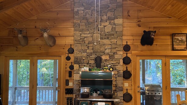 Interior rústico de una cabaña con pared de piedra, vigas de madera, chimenea y una decoración de oso.