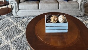 A living room with a grey sofa, two blue pillows, a wooden coffee table with decorative items, a kitchen in the background, and a sign that reads "LAKE HOUSE". - Beautiful Land's End Waterfront Condo (Osage Beach)