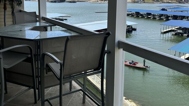 A covered patio with a table and chairs, overlooking a marina with boats and docks. - Beautiful Land's End Waterfront Condo (Osage Beach)