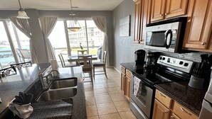 A modern kitchen with wooden cabinets, a black countertop, and a large window overlooking a balcony. - Beautiful Land's End Waterfront Condo (Osage Beach)