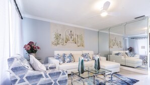 A modern living room with a white sofa, patterned armchair, and a glass coffee table. There is a large mirror reflecting the room and a painting on the wall. - PALM BEACH GARDENS  GUEST HOUSE (Palm Beach Gardens)