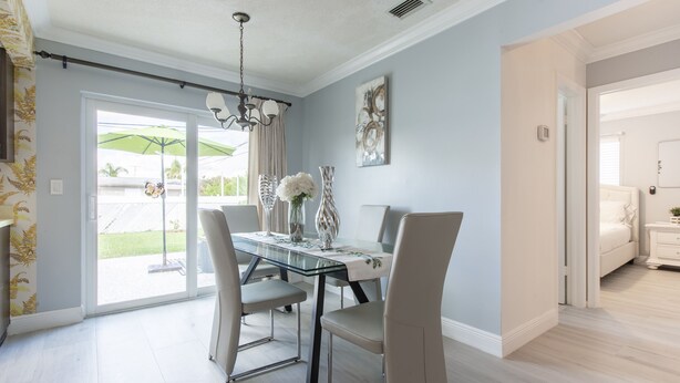 A dining area with a glass table, chairs, and a chandelier. There is a door leading to another room. - PALM BEACH GARDENS  GUEST HOUSE (Palm Beach Gardens)