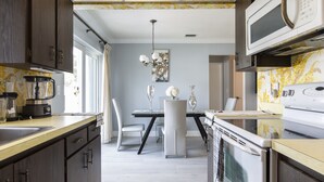 A modern kitchen with dark wood cabinets, a white countertop, and a dining area with a white table and chairs. - PALM BEACH GARDENS  GUEST HOUSE (Palm Beach Gardens)